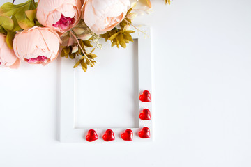 Holiday card for Valentine's Day. White frame, red glass hearts, a bouquet of pink flowers on a white background. Copyspace.