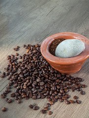 Black coffee ground in a clay mortar and in grains on the surface of a wooden table in sunny rays, with place for text.