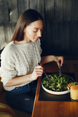 Girl eats vegetable salad. Lady sitting in a cafe. Brunette in a white sweater.