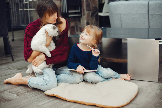 Beautiful mother with little daughter. Family sitting in the room. Cute girl doing homework. Woman playing with kitty