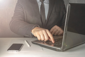 Man male businessman in a suit with a tie works at a laptop on a table with a sheet of paper, a pen...