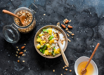 Greek natural yogurt with tropical fruits and granola on a dark background, top view. Natural yogurt with kiwi, mango and  peanut butter granola