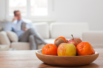 Mature man sitting with smartphone in a living room with fruit bowl in the foreground