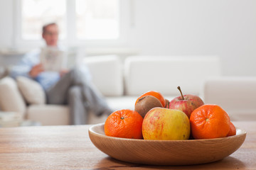 Mature man reading a newspaper in a living room with fruit bowl in the foreground