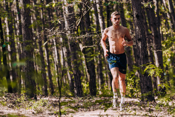 Shot of sporty shirtless young man running on mountain path in beautiful nature with trees