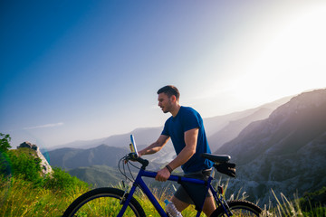 Fototapeta premium Perspective of a fit mountain biker pushing his bike uphill with amazing view on a forest, river and mountains in the background. Amazing green nature at sunset.