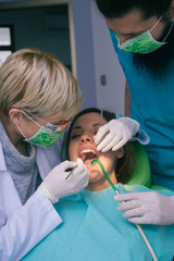 Professional male and female dentists examining woman's teeth in dental office