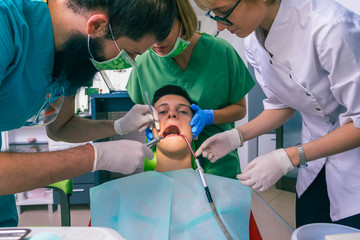 Team of dentists treating the teeth of their young boy patient using their dental tools.