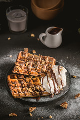 Plate of belgian waffles with chocolate sauce and ice cream on dark background