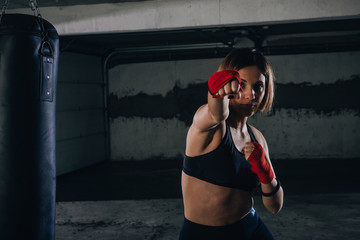 Young beautiful female preparing her bandages for kicking the boxing bag