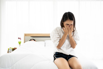 Worried woman sitting on the bed while her husband sleeping.