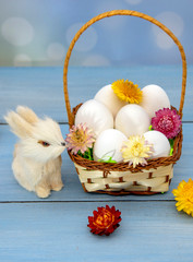 The Easter Bunny sits next to a basket full of eggs, decorated with dried flowers.