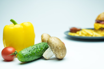 Vegetables near hamburger and blurred french fries on white background