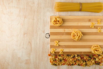 fettuccine and Farfalle are laid out on a bamboo cutting Board and with other macaroni on a wooden background