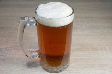 Glass goblet with a handle of fresh dark beer with foam on a wooden table