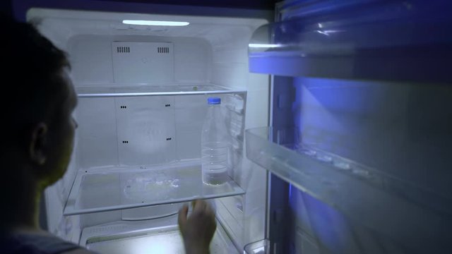 Man Looking For Food In The Fridge. The Guy Puts Milk Into The Empty Fridge. Night Hunger. Hangover. Bachelor's Fridge. A Dirty Fridge Without Any Food.