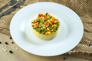 Healthy vegetarian food - porridge couscous with steamed vegetables on a white ceramic plate on rustic background. Tasty food flat lay
