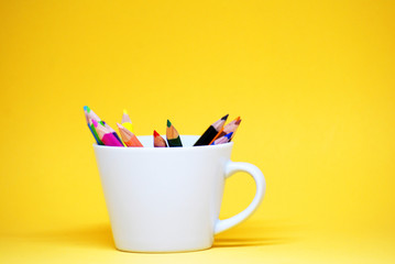 Coloured pencil or colorful Crayon for drawing on the white cup isolated with yellow pastel background Back to school concept 