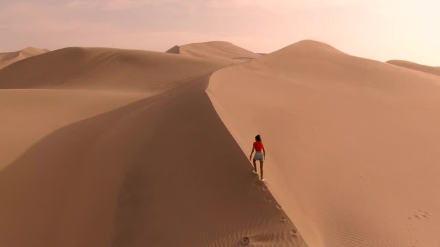 Woman in Sandy desert oasis lake. DRONE. Water in middle of hot sand desert. Romantic, holiday, honeymoon, scenic view, sand ripples and footprints. Tourism. Huacachina, Peru. Epic, dramatic shot. 