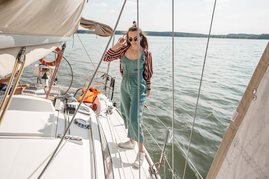 Girl staying on the sailboat. Woman in nice outfit and sunglasses relaxing on a cruise boat. Young beautiful woman embracing on the yacht on vacation.