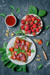 Strawberry toasts with mint and jam on grey cement background top view. Bright colourful summer vegetarian food.