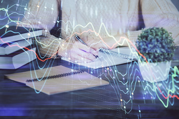 Forex graph on hand taking notes background. Concept of research. Double exposure