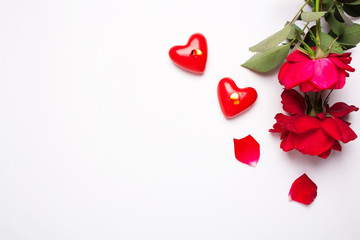 Red roses and two red candles in the shape of a heart for Valentine's Day on a white background