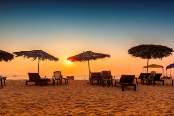 Sun umbrellas with lounge chairs at sunset on a tropical sunny beach in GOA, India - obrazy, fototapety, plakaty