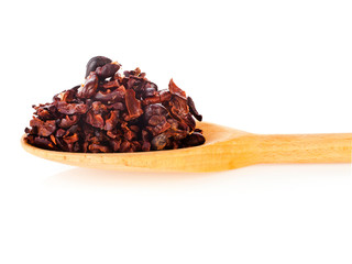 Cacao nibs in a wooden spoon isolated on a white background.