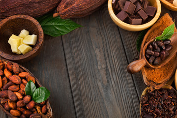Cacao beans and powder, cacao butter and cacao nibs with chopped chocolate on a wooden background. Text space.
