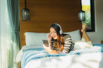 Portrait young asian woman using smart mobile phone with headphone for listen music in bedroom