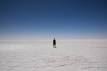 Lonely man walks alone into the endless dry salt lake of Uyuni