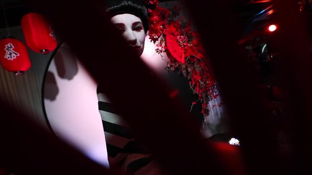 Japanese geisha in traditional makeup and clothes with a fan in his hands