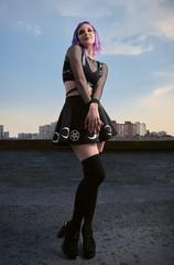 Portrait of cute smiling gothic girl on roof at sunset time. Pastel goth with violet (purple) hair...