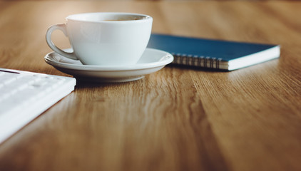 Close up white coffee cup with notebook and computer keyboard on desk