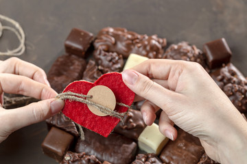 Appetizing food background. Assortment of chocolate handmade candy and red heart card for valentine's day in female hands. Chocolate background.  