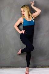 The concept of one fitness. Full-length photo of a pretty slender blonde woman athlete in a tracksuit on a gray background. Standing in different poses with emotions and a smile.