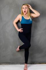 The concept of one fitness. Full-length photo of a pretty slender blonde woman athlete in a tracksuit on a gray background. Standing in different poses with emotions and a smile.