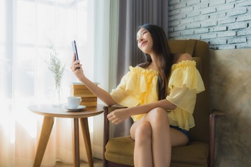Portrait young asian woman using mobile phone with coffee cup and read book sit on chair in living room