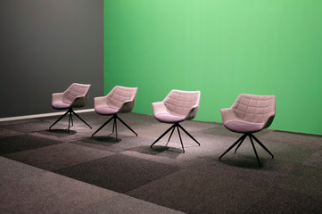 Four empty chairs in a TV studio with green screen background