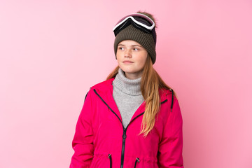 Ukrainian teenager skier girl with snowboarding glasses over isolated pink background standing and looking to the side