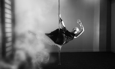 The dancer on the pylon in the studio. Girl doing exercises on a sports equipment.