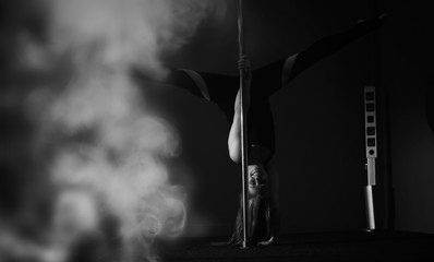 The dancer on the pylon in the studio. Girl doing exercises on a sports equipment.