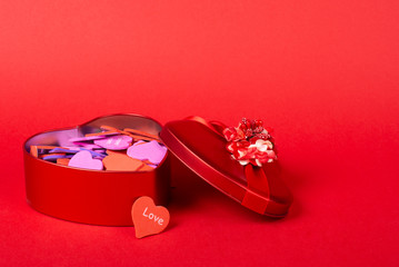 Red heart-shaped gift box with a ribbon full of multicolored handmade paper hearts on a bright red background (copy space on the right for your text, Valentine Day concept)