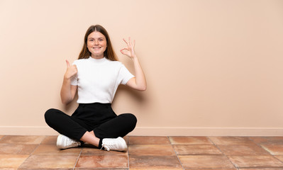 Fototapeta na wymiar Ukrainian teenager girl sitting on the floor showing ok sign and thumb up gesture