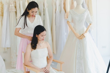 The bridesmaid is helping the beautiful bride wearing a white wedding dress in front of the mirror.