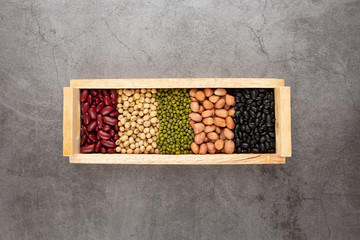 Grains or beans, red bean, black bean, green bean, soybean, peanut in the wooden tray placed on the black cement floor. Top view.