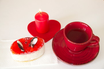 Valentine's Day. On a white background is a red ceramic cup with tea and saucer, a cake, a red candle and a decorative felt heart.