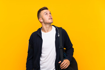 Young blonde sport man over isolated yellow background looking up while smiling