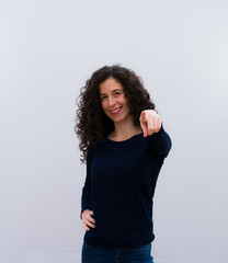 young pretty woman laughing at you, pointing to camera and making fun of or mocking you against white wall